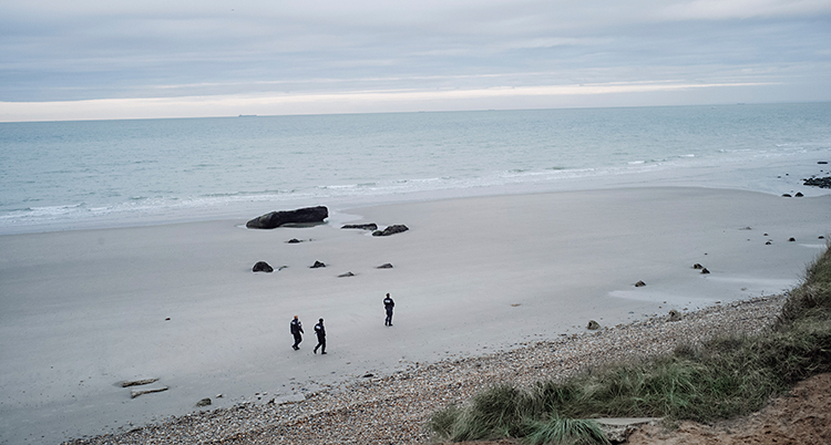 Tre poliser går på en strand vid havet.