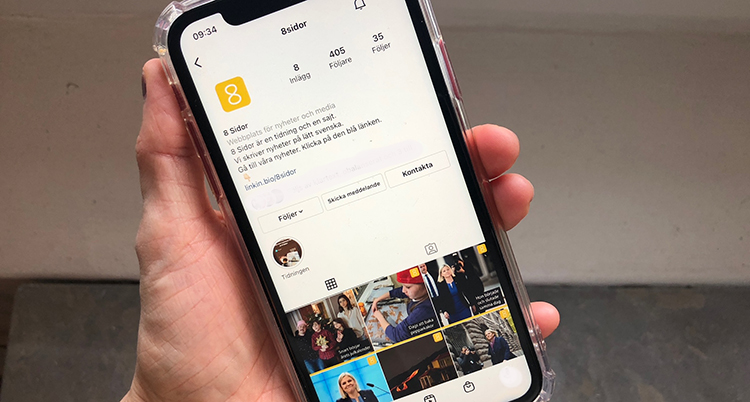 En hand håller i en mobil. På skärmens syns 8 Sidors sida på Instagram.