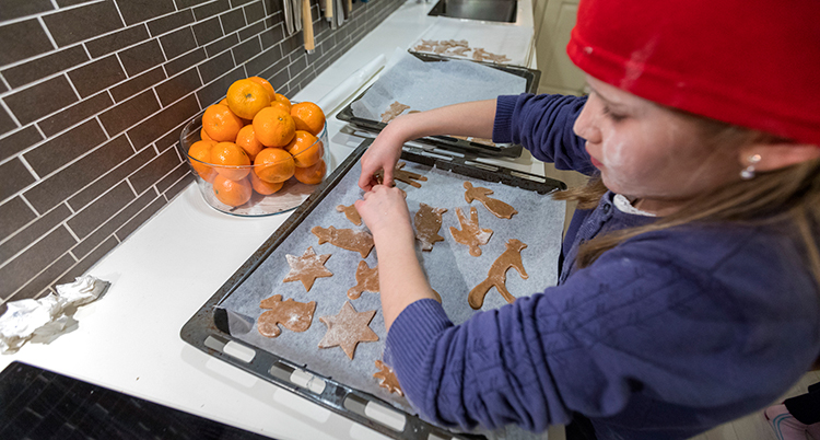 Ett barn står vid spisen med en plåt pepparkakor
