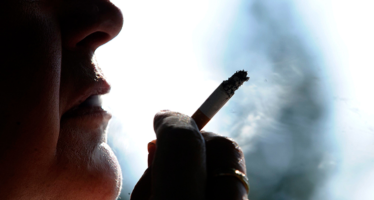 En hand håller en rykande cigarett nära ansiktet