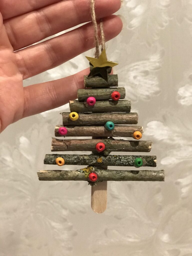 En hand håller i pyntet som ser ut som en liten julgran av pinnar och pärlor.