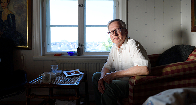 Han har vit skjorta och tittar in i kameran. Bakom honom syns ett fönster.