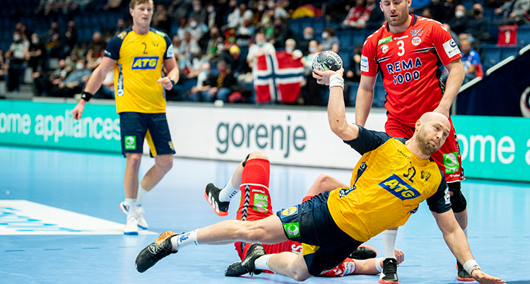 Han hoppar upp i luften med uppsträckt högerarm, håller i en boll och ska skjuta. Flera motståndare sträcker upp armarna för att försvara