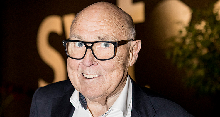 Han ler och tittar in i kameran. Han har glasögon på sig.