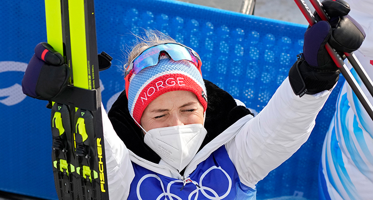 Johaug sträcker armarna i luften. Hon har munskydd.