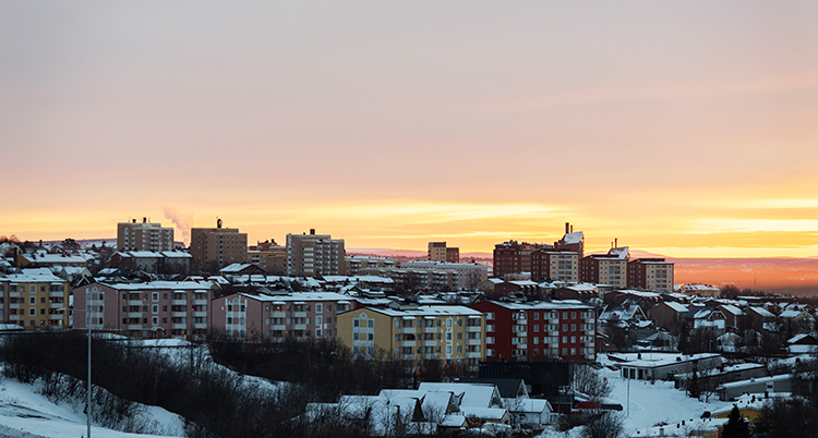 Bakom en kulle med hyreshus är himlen rosagul.