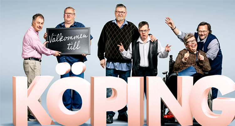 Sex personer står och sitter bakom en rosa skylt