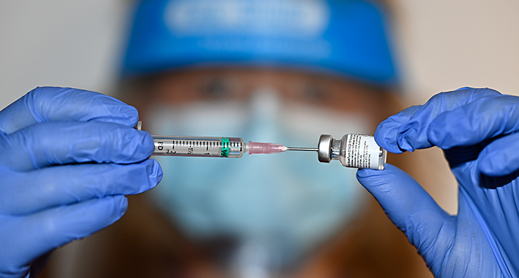 En närbild på två händer. Ena handen håller en spruta. Andra handen håller en liten glasburk med vaccin.
