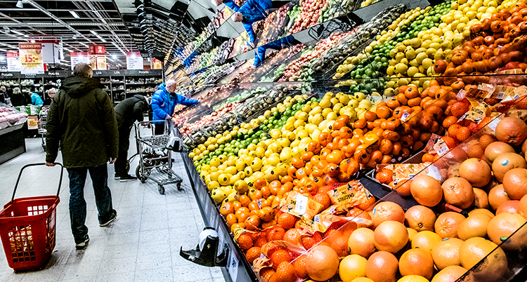 Människor går med varukorgar i en butik vid en hylla för frukt.