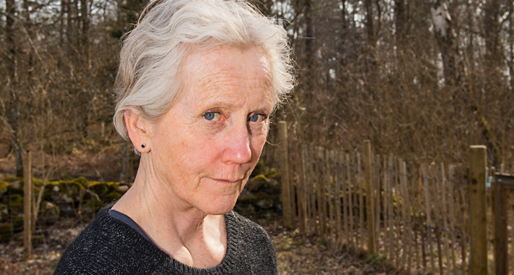 Hon tittar in i kameran och ser allvarlig ut. I bakgrunden är en skog.