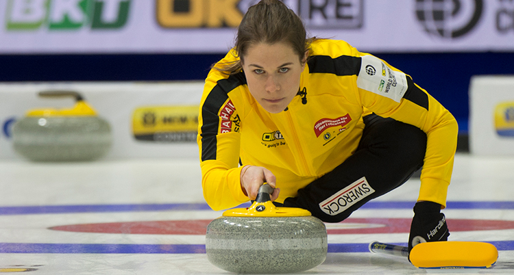 Hon hukar ner på isen och är på väg att skjutsa iväg en curlingsten på isen.