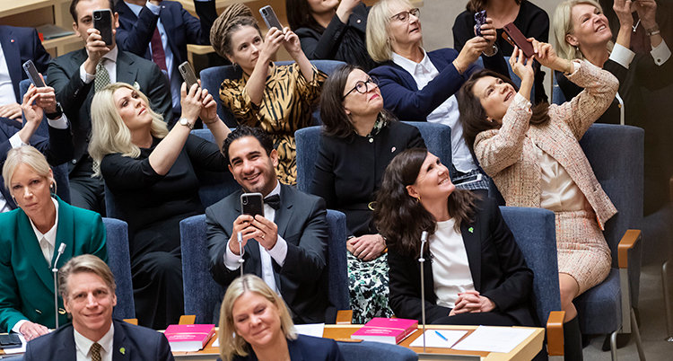 De sitte ri bänkarna i riksdagen och håller upp sina mobiler för att ta bilder. Längst fram syns Magdalena Andersson