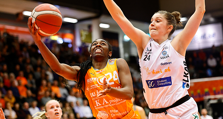 Från en match i basket. En kvinna med orange linne försöker med ett skott.