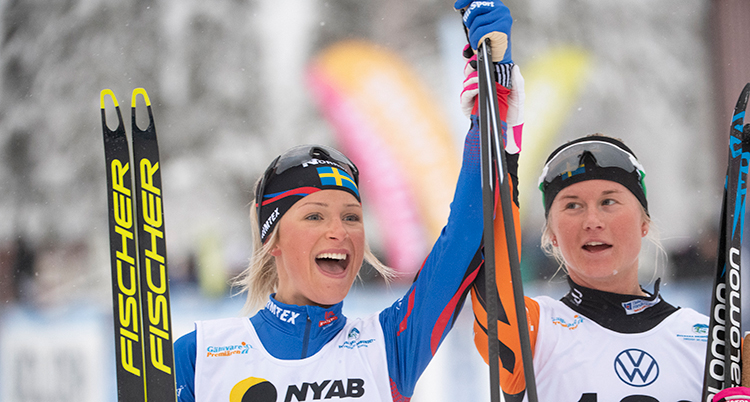 De håller i sina skidor och sträcker upp varandras händer i luften.