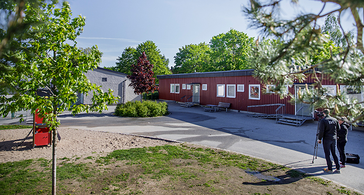 Det är soligt utomhus. Två personer med en kamera står utanför ett hus.