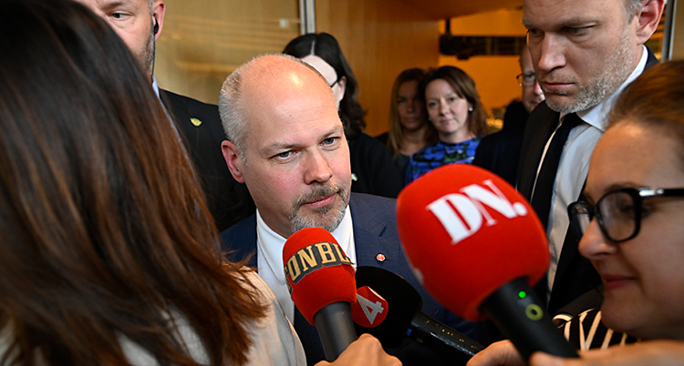 Han är i riksdagens hus. Många journalister sträcker fram sina mikrofoner mot honom.