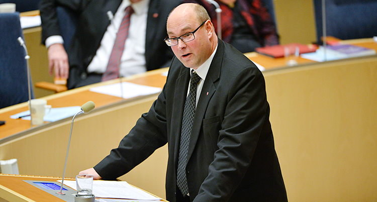 Han står och pratar i talarstolen i riksdagen.