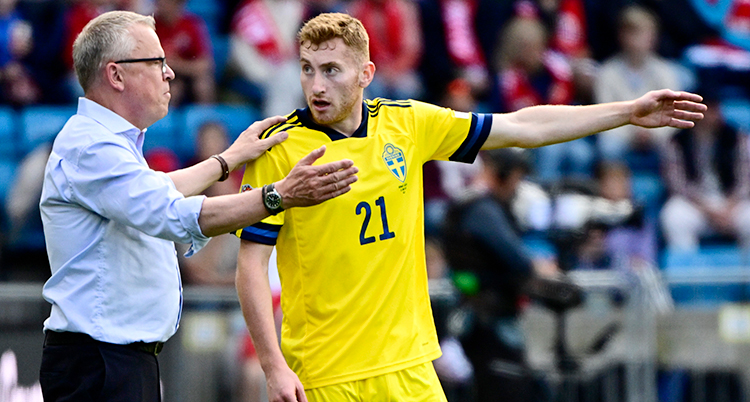 Fotbollsspelare i gul landslagströja pratar med sin tränare.