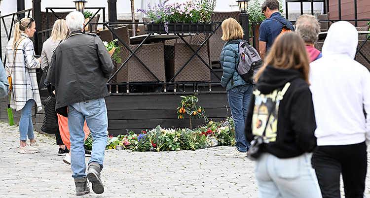 Flera människor står vid en uteservering. På marken ligger massor av blommor.