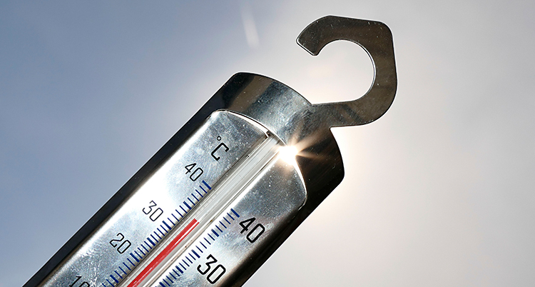En termometer visar 34 grader. I bakgrunden lyser solen.