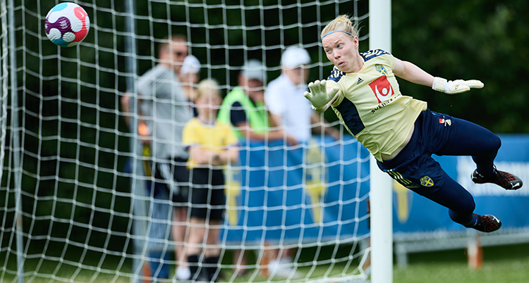 En kvinnlig fotbollsmålvakt räddar en boll.