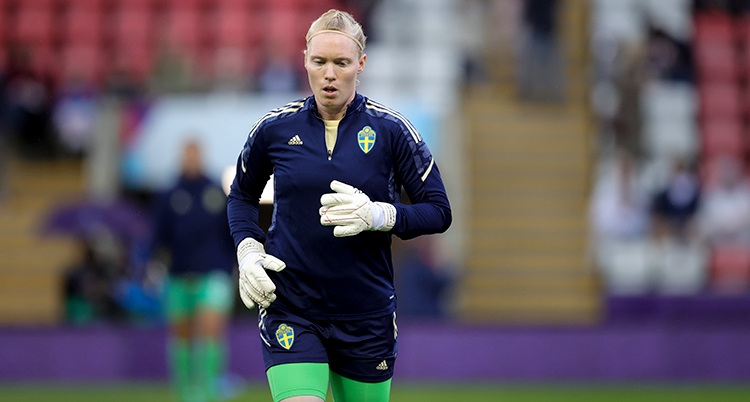 Kvinnlig fotbollsmålvakt med stora vita handskar värmer upp.