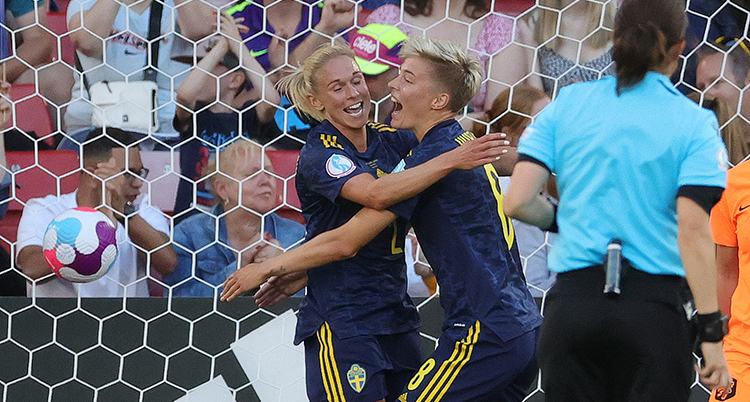 Två fotbollstjejer i landslagsdress kramar om varandra.