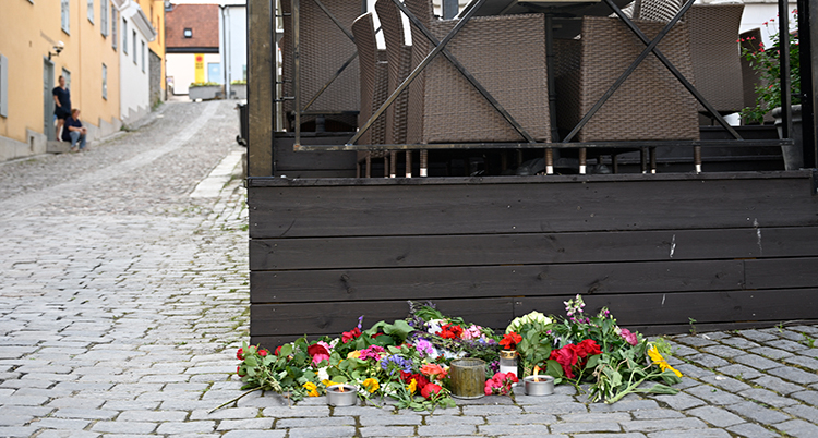 Det ligger blommor på kullersten och mot en altan i trä.