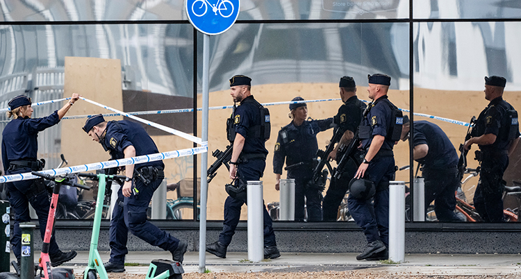 Flera poliser står vid en väg. En går under en avspärrning.