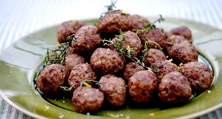 Många stekta köttbullar ligger på en grön tallrik. Timjan ligger på som dekoration.