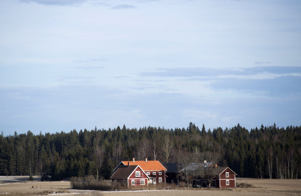 Två röda huset vid en åker. I bakgrunden syns skog.