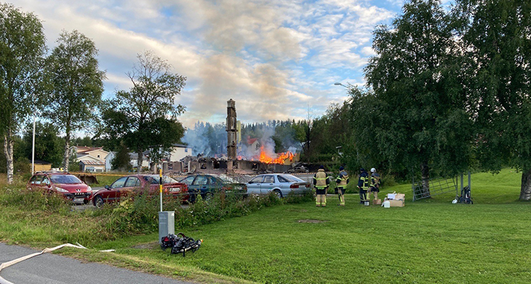 Det är dag och grunden av huset brinner fortfarande. En brandslang ligger på marken.