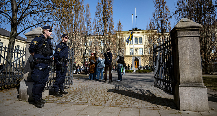 Två poliser står vid en grind. Längre fram syns en gammal skola.