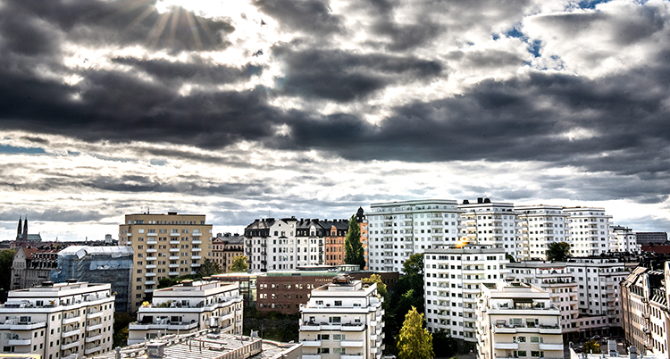Solen tittar fram bland molnen över en stad med många lägenheter.