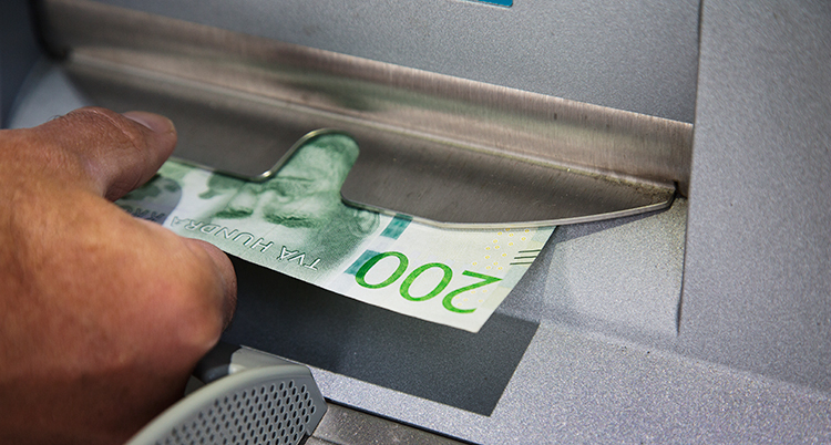 En hand med en sedel vid en bankomat.