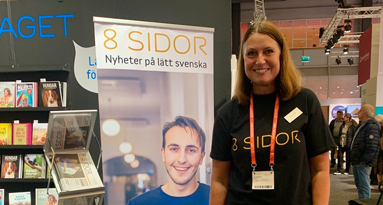 Hon står vid en skylt för 8 Sidor.