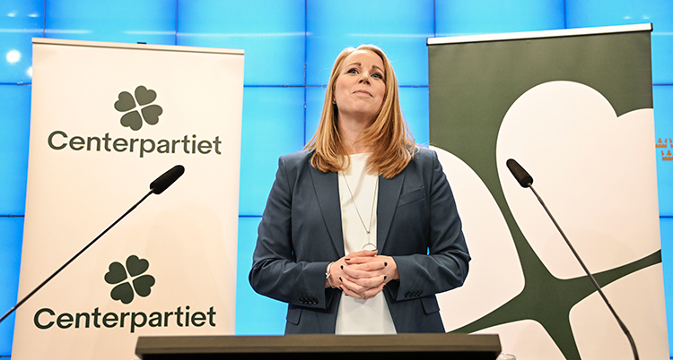 Hon står vid en scen med mikrofoner och Centerpartiets flaggor.