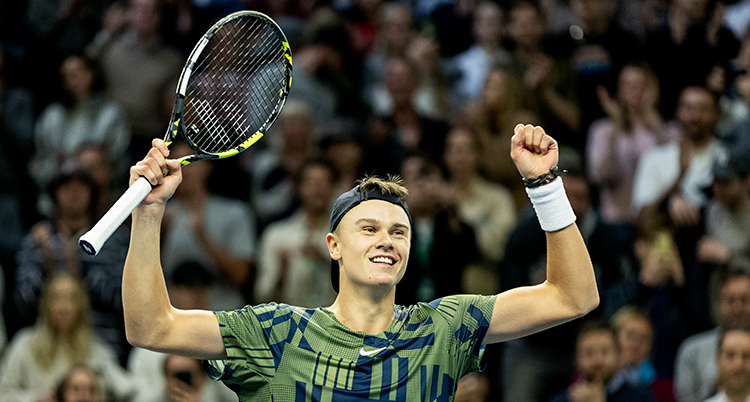 Han är glad. Han sträcker armarna upp i luften. I ena handen håller han ett tennisrack. Bakom syns publik.