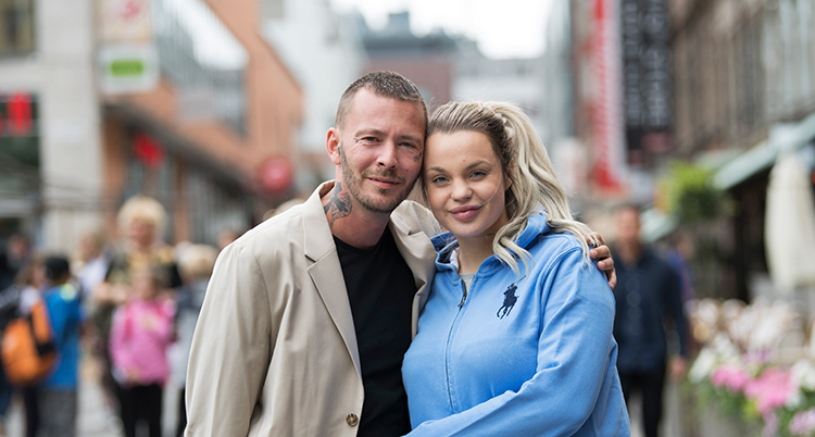 Jocke och Jonna står på en gågata. De lutar huvudena mot varandra.