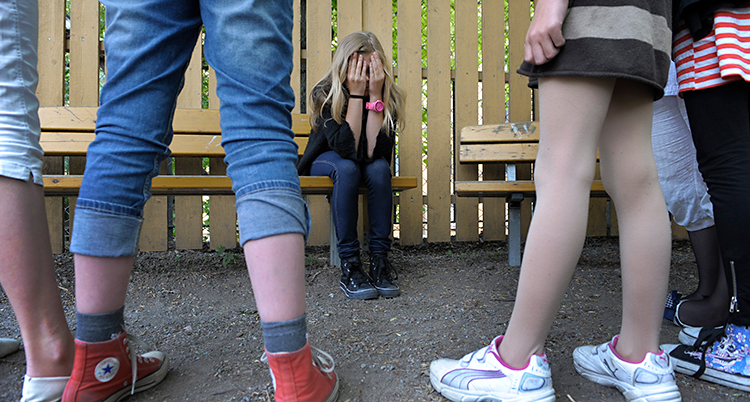 En tjej sitter med händerna i ansiktet. Flera andra står runt henne.
