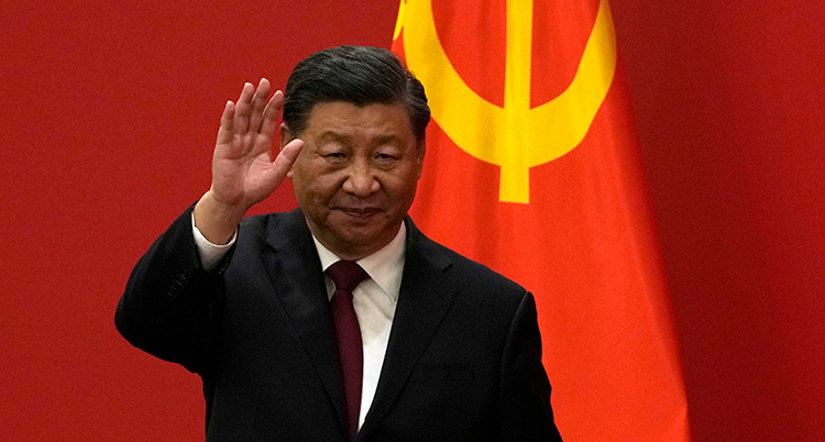 Xi Jinping vinkar. Han står framför en röd fond och Kinas flagga.