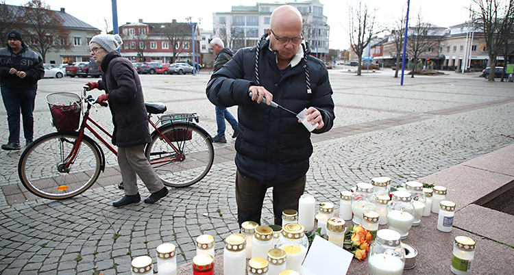 En man står på ett torg och tänder ett ljus. Det finns flera lyktor med ljus vid honom.