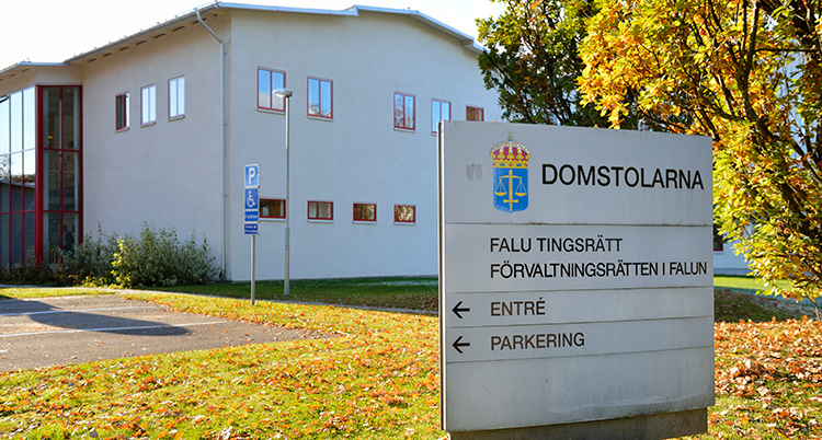 Falu tingsrätt syns som ett vitt stort hus i bakgrunden. En skylt i förgrunden med texten Domstolarna och pilar till bland annat en parkering.