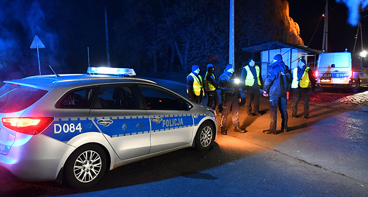 En polisbil och flera personer i reflexvästar framför polisbilen. Det är mörkt ute.