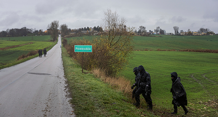 tre personer i regnkläder går vid ett fält vid en väg.