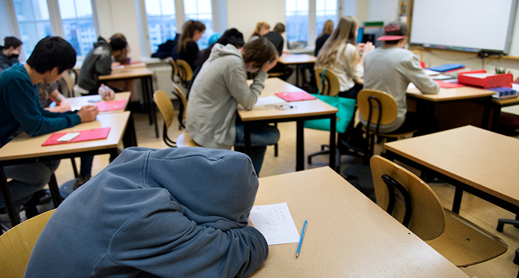 Ett klassrum med elever. I förgrunden en elev som lutar huvudet mot bordet.