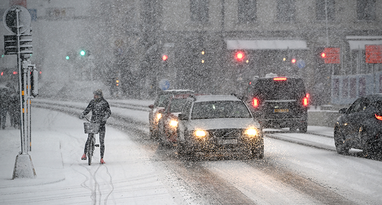 En snöig gata med en cyklist och flera bilar.