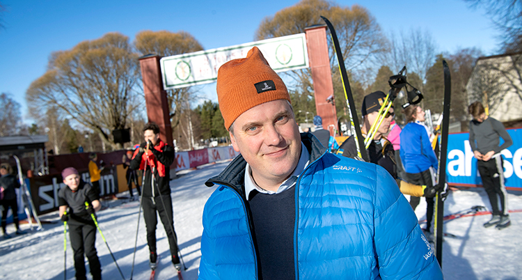 Han står utomhus i en blå jacka och en brun mössa. Bakom syns Vasaloppets mål.