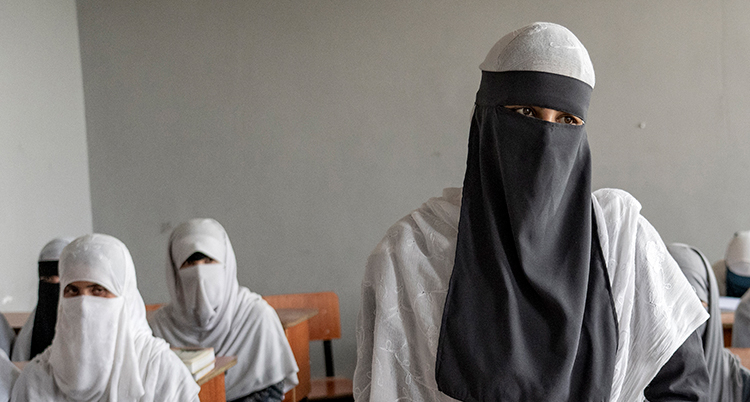 De är klädda i burka och sitter vid bänkar.