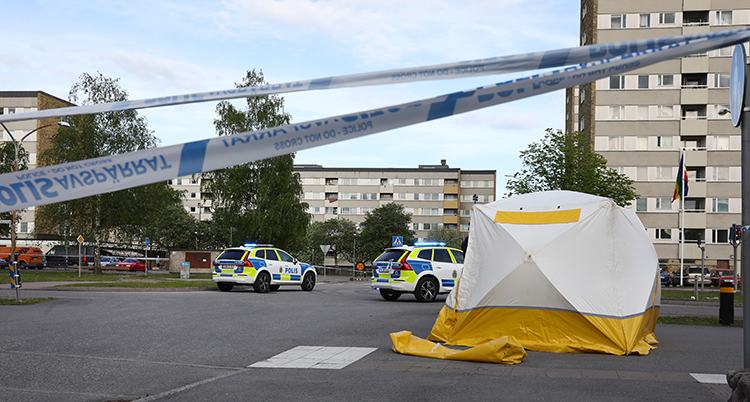 Avspärrningsband syns i förgrunden. Hyreshus syns bakom. På gatan står ett vitt tält.